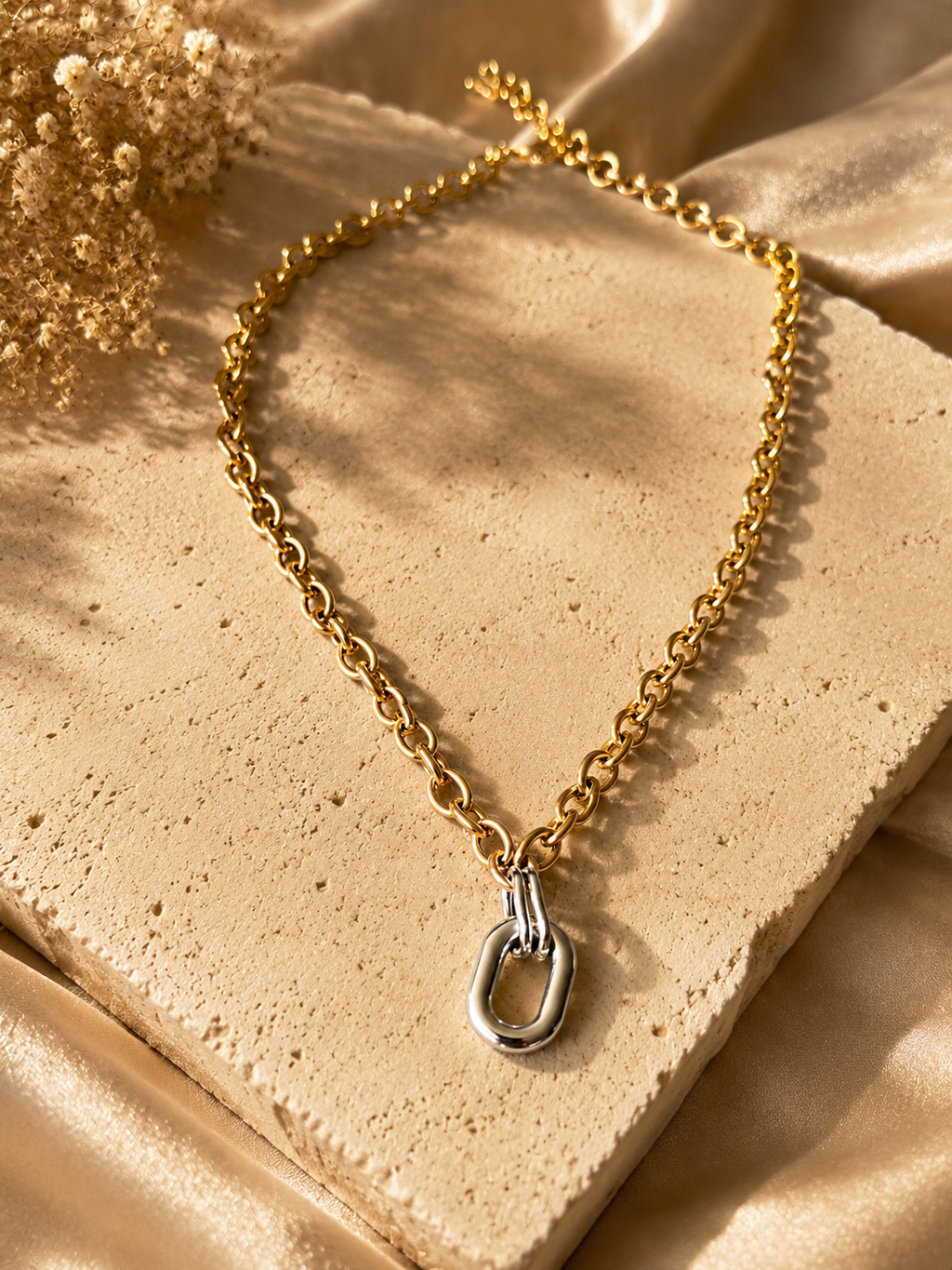Two-tone link pendant necklace displayed on stone and gold satin