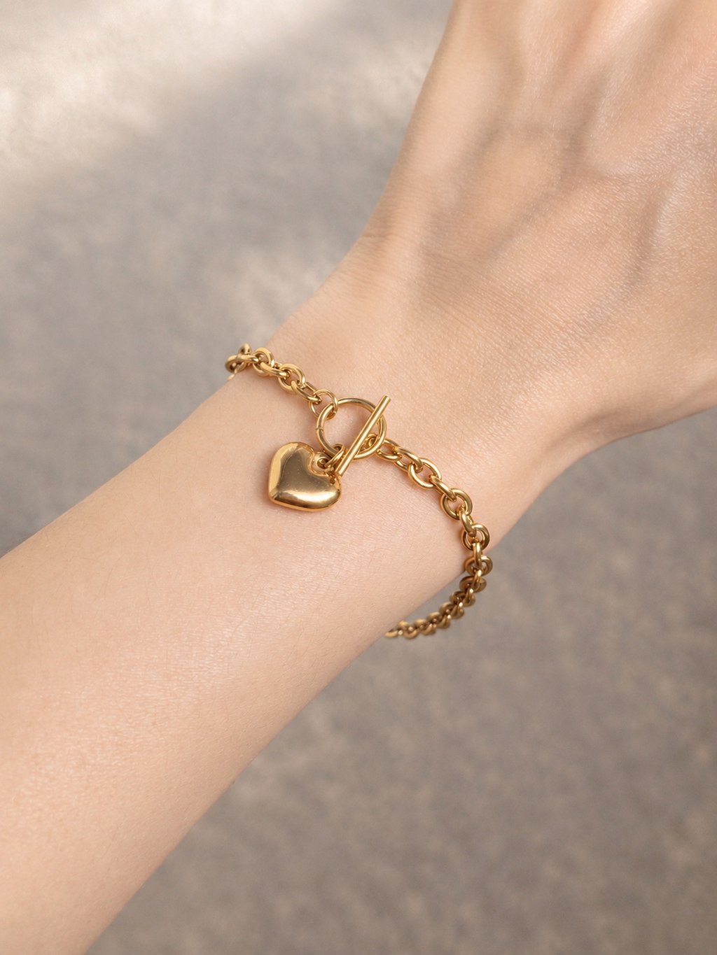 Gold-tone heart charm bracelet with toggle clasp worn on wrist