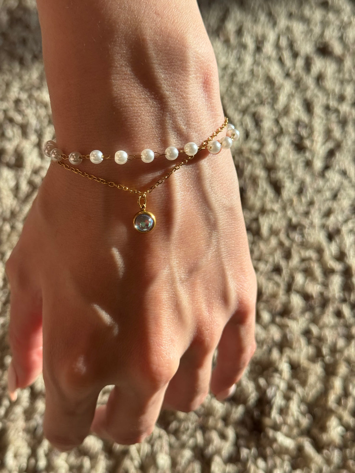 Faux-pearl and gold-tone charm bracelet worn on hand in sunlight