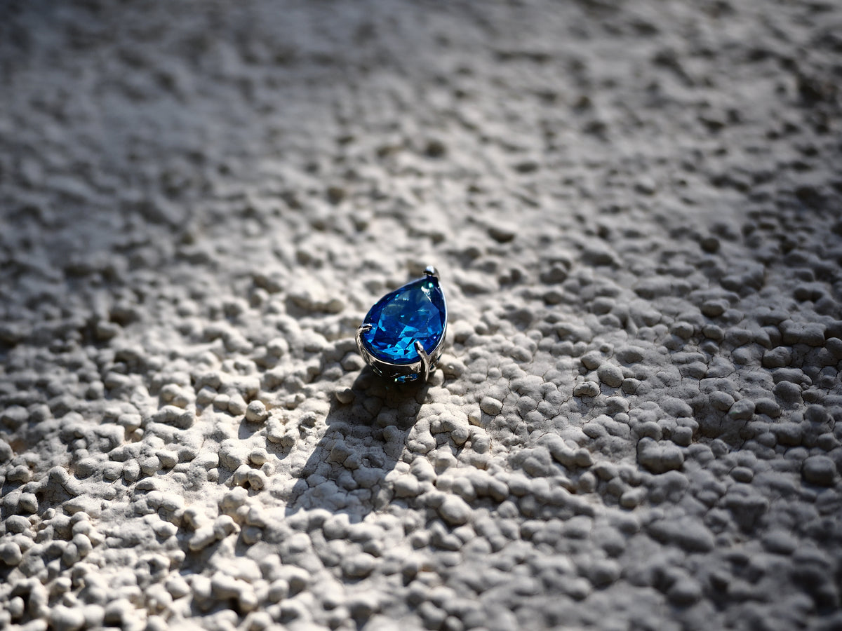 Deep blue pear-cut cubic zirconia pendant photographed on textured stone