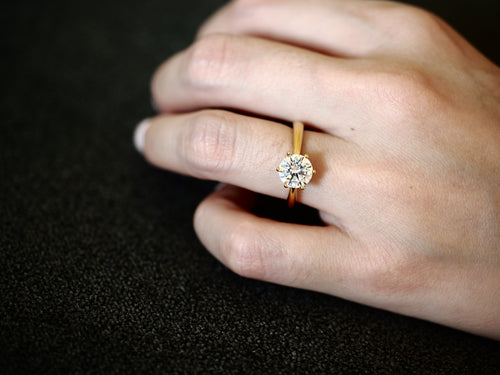 Gold-tone cubic zirconia solitaire ring worn on hand