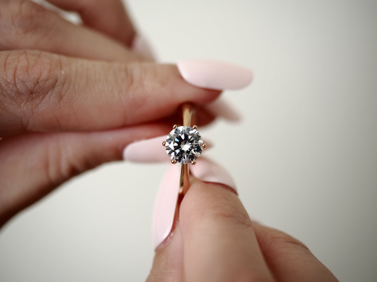 Rose gold-tone cubic zirconia solitaire ring held between fingers