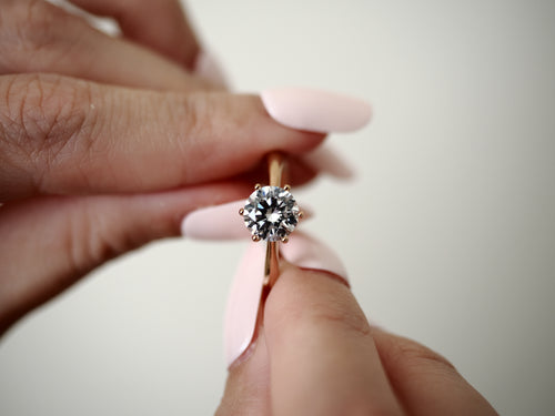 Rose gold-tone cubic zirconia solitaire ring held between fingers