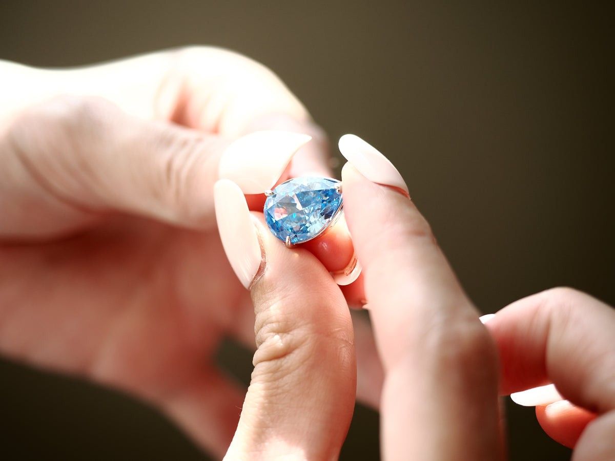 Light blue pear-cut cubic zirconia pendant held between fingers