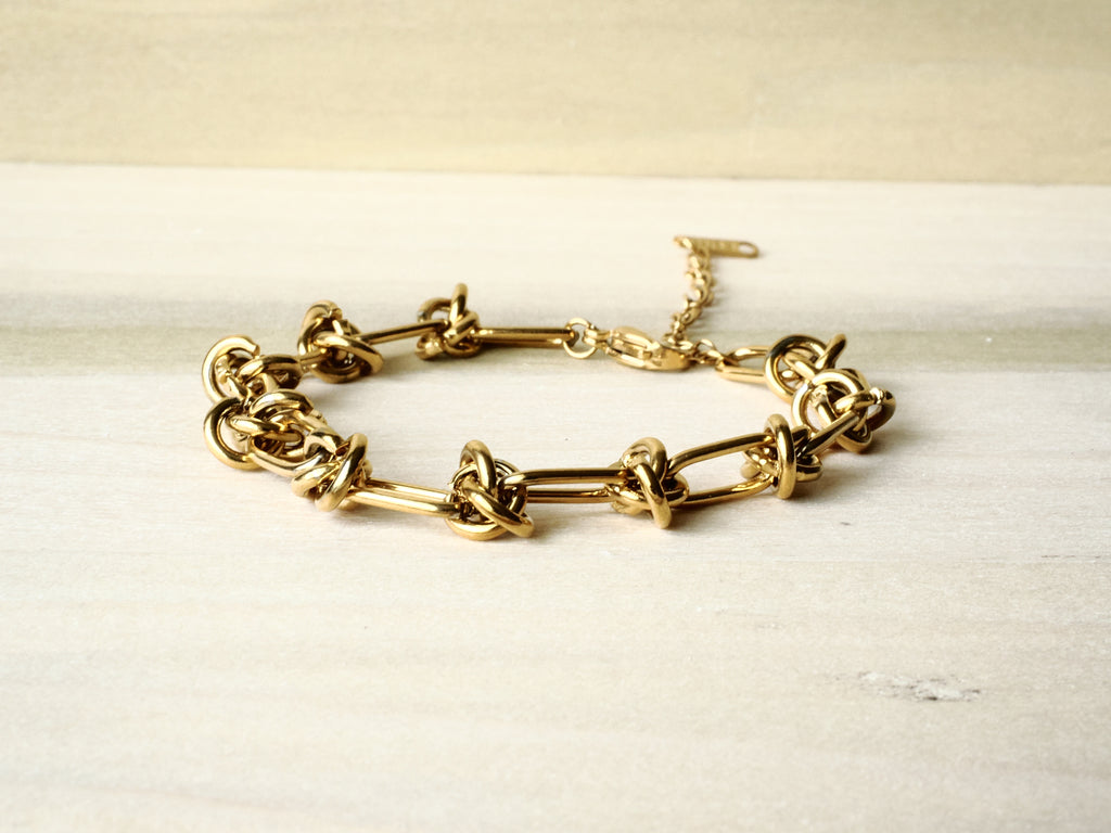 Gold-tone Knot Link bracelet arranged on cream fabric