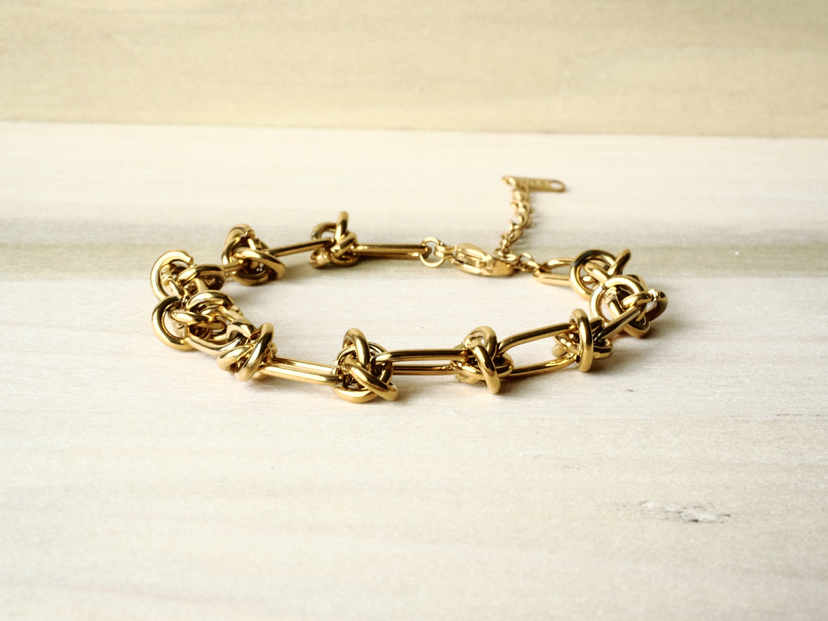 Gold-tone Knot Link bracelet arranged on cream fabric