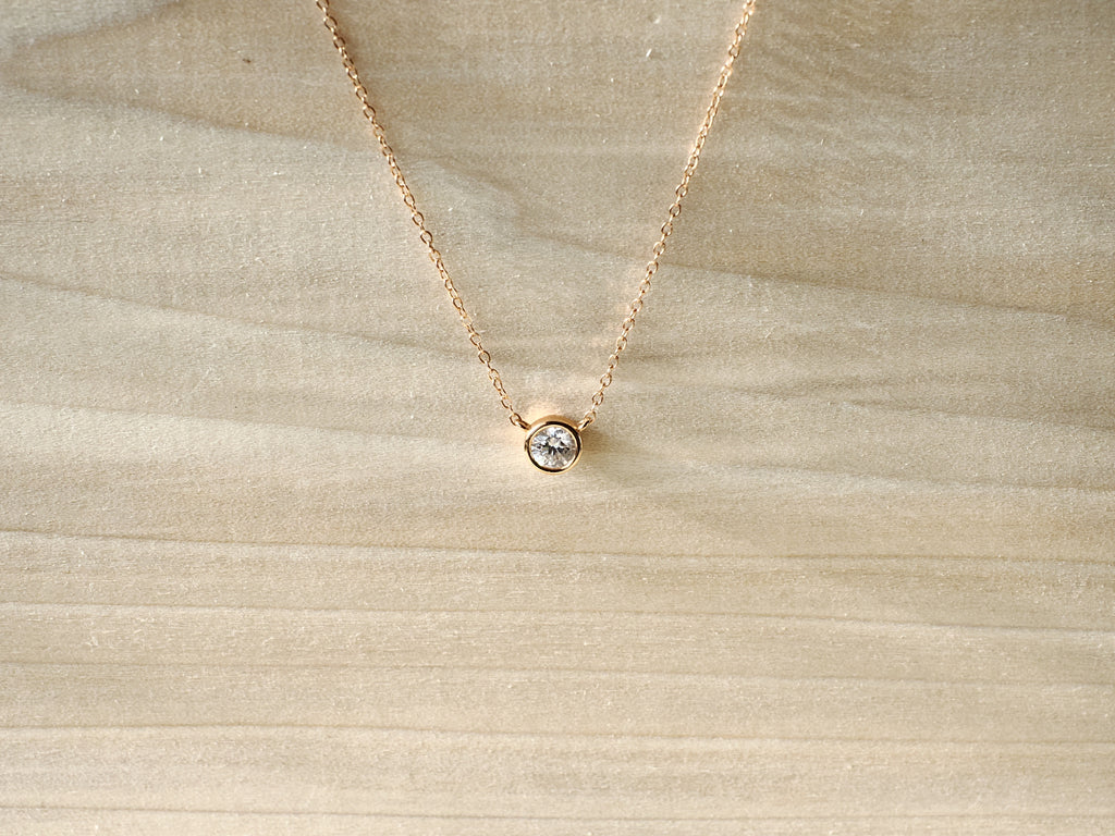 Rose-gold-tone necklace with round bezel-set stone on cream fabric